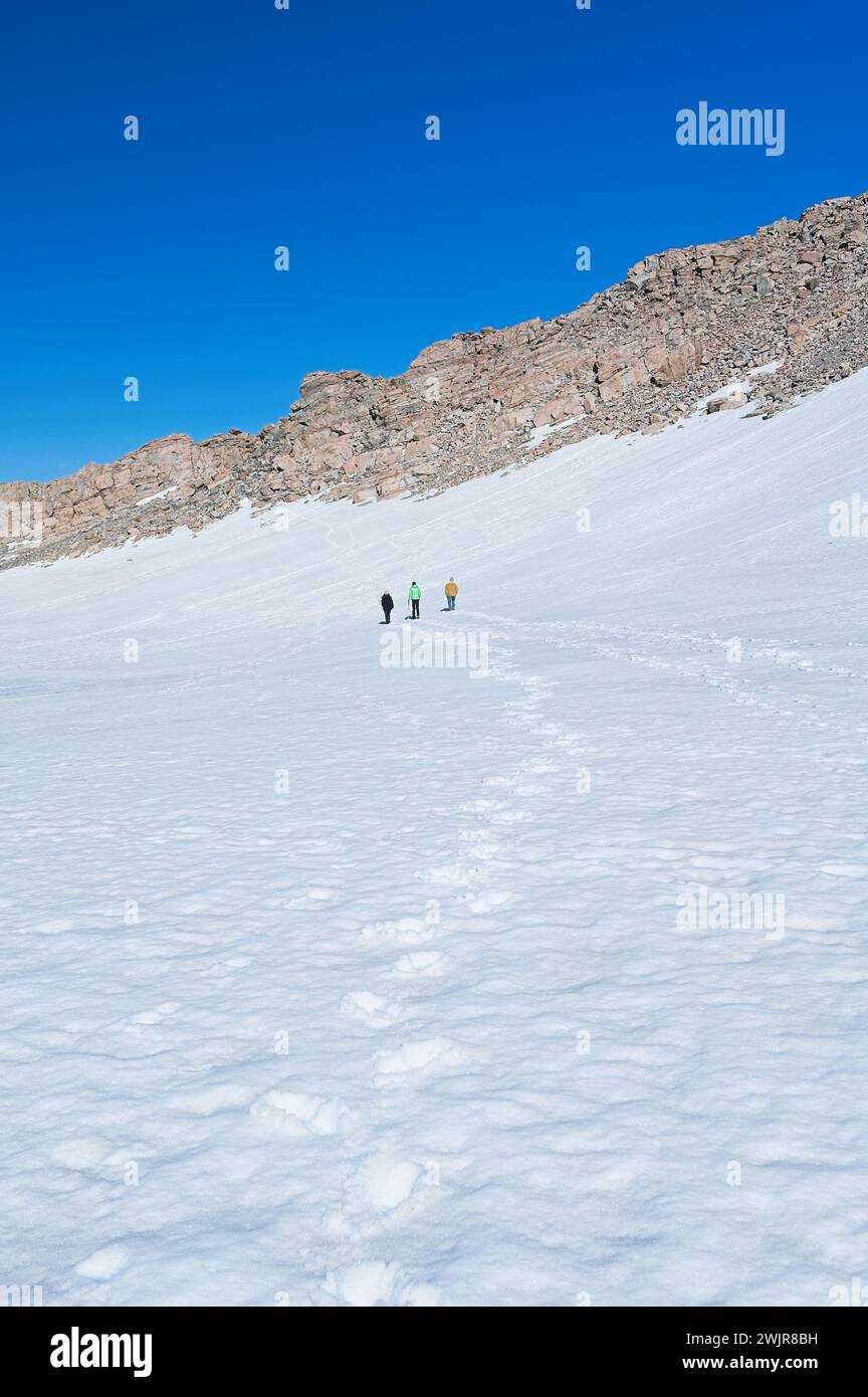 Eine Gruppe von Menschen wird durch eine schneebedeckte Landschaft, umgeben von Gletscherlandschaften und dem eisigen Winterhimmel, beobachtet Stockfoto