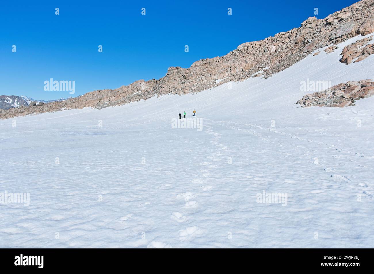 Eine Gruppe von Menschen wird durch eine schneebedeckte Landschaft, umgeben von Gletscherlandschaften und dem eisigen Winterhimmel, beobachtet Stockfoto