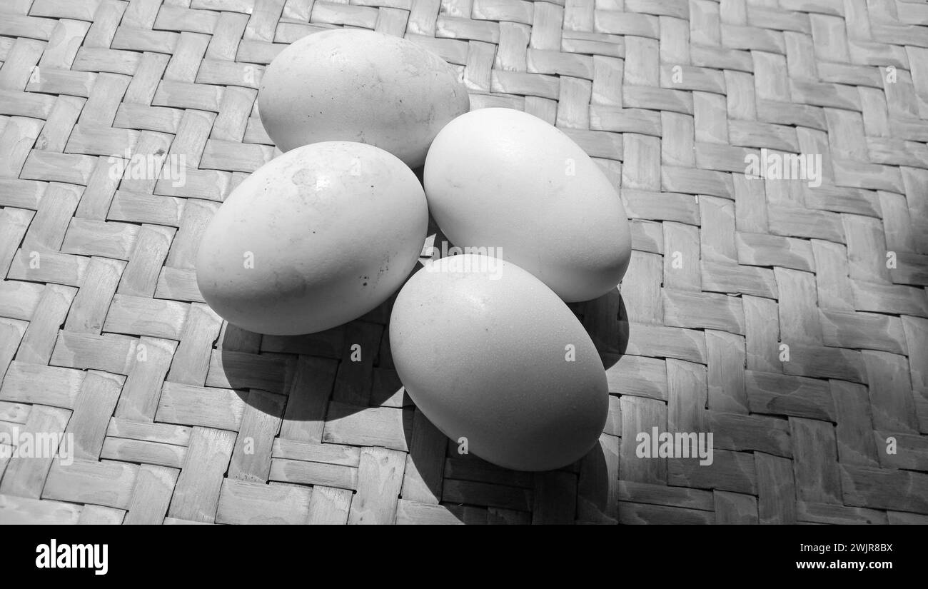 Foto von 4 Hühnereiern auf einem Schwarz-weiß-Motiv auf einem Hintergrund aus gewebtem Bambus Stockfoto