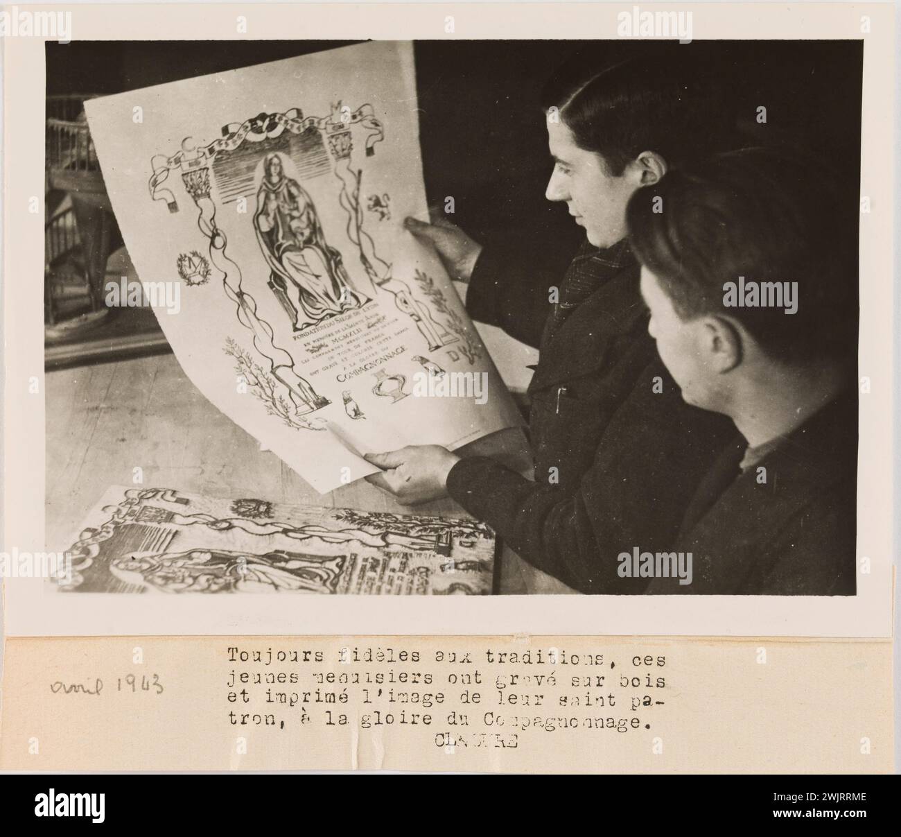 Gamet, André. Propagandafotografie: Zwei Gefährten, die sich einen Druck ansehen. Immer den Traditionen treu, diese / jungen Zimmerleute auf Holz gravieren / und drucken das Bild ihres heiligen PA- / tron, zum Ruhm der Gemeinschaft. Gelatino-Silberbromid-Entnahme. Daktylographische Legende in schwarzer Tinte. 1943-04-1943-04. Paris, Carnavalet Museum. 144781-9 Stockfoto