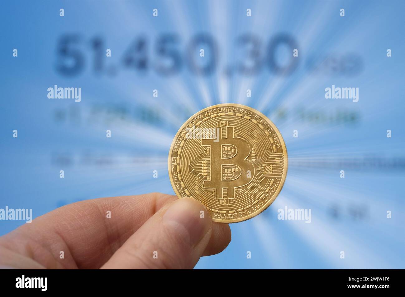 Bitcoin-Münze zwischen den Fingern vor einem Marktpreis von über 50.000 USD Stockfoto