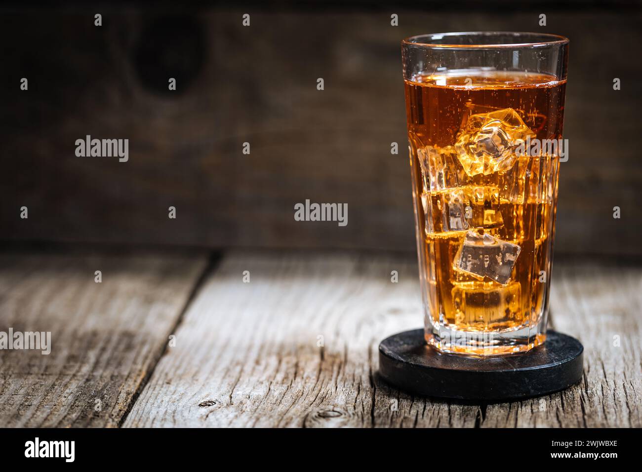 Eistee mit viel Eis in transparentem Glas auf rustikalem Holztisch Stockfoto