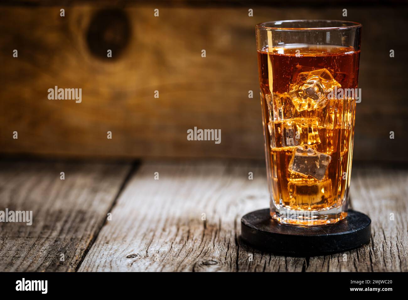 Eistee mit viel Eis in transparentem Glas auf rustikalem Holztisch Stockfoto