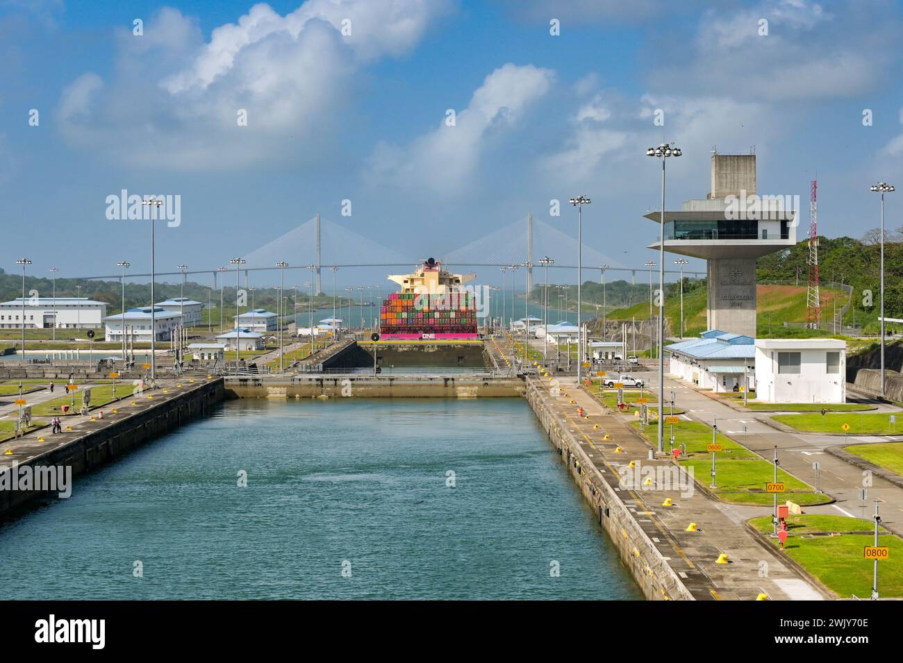 Colon, Panama - 23. Januar 2024: Schleusen und Kontrollturm von Agua Clara am Panamakanal. Im Hintergrund befindet sich ein Containerschiff und die Atlantikbrücke Stockfoto