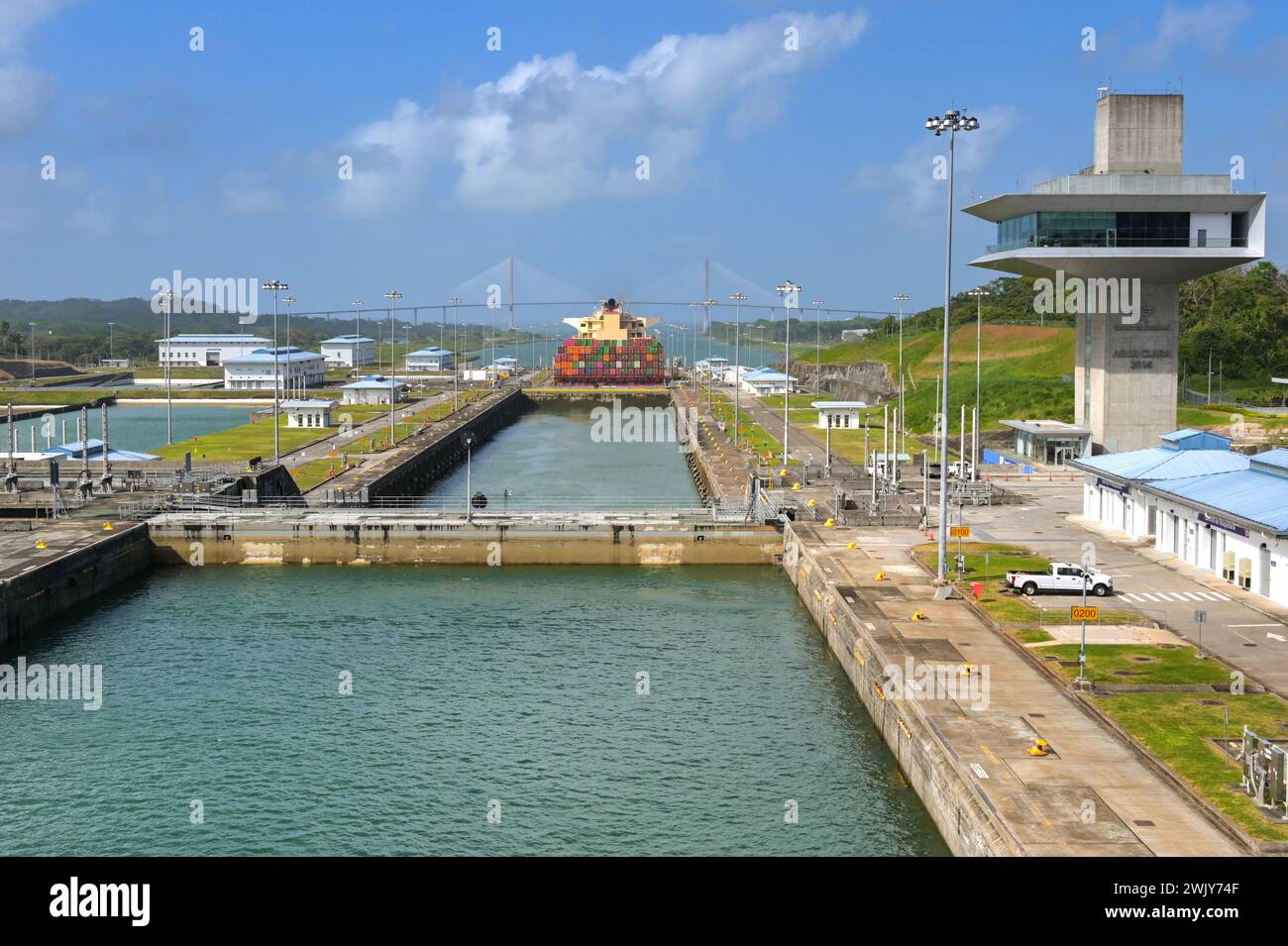 Colon, Panama - 23. Januar 2024: Schleusen und Kontrollturm von Agua Clara am Panamakanal. Im Hintergrund befindet sich ein Containerschiff und die Atlantikbrücke Stockfoto