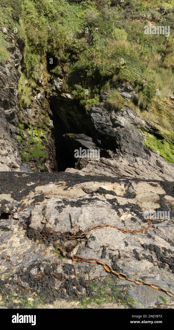 Rostige Ankerkette auf Felsen vor einer Höhle in Cornwall, Großbritannien Stockfoto