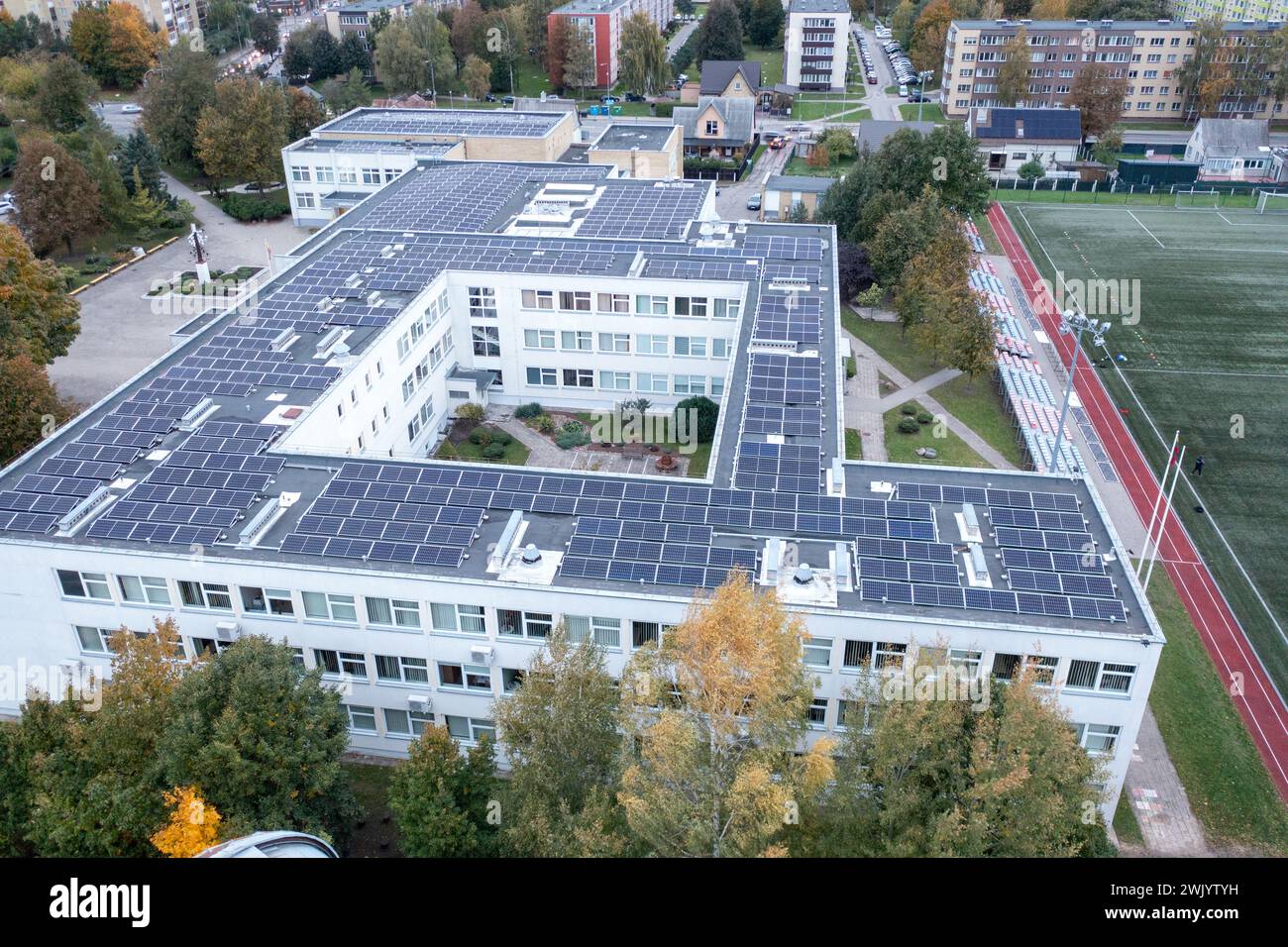 Drohnenfotografie des Schulgebäudes mit Solarpaneelen auf dem Dach am herbstlichen sonnigen Abend Stockfoto