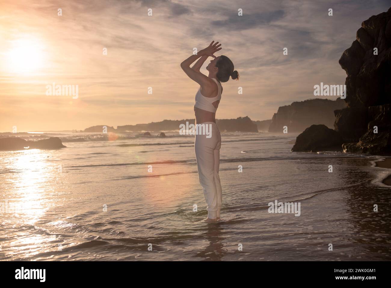 Frau, die am Strand steht und bei Sonnenaufgang und Sonnenuntergang meditiert Stockfoto