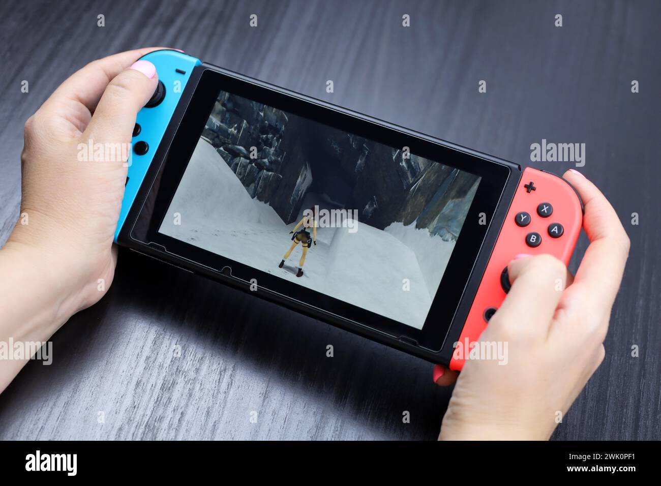 Mädchen spielt Tomb Raider Remastered mit Lara Croft-Spiel auf der Nintendo Switch-Konsole im Handheld-Modus, selektiver Fokus auf einem Bildschirm Stockfoto