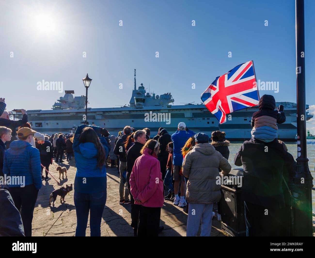 Ein Junge, der auf den Schultern seines Vaters sitzt, winkt einen Union Jack, während der Flugzeugträger der Queen Elizabeth-Klasse „HMS Prince of Wales“ von Portsmouth Harbour abfährt Stockfoto