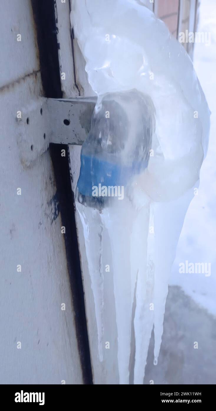 Ein Vorhängeschloss an einer Metalltür vor einem Gebäude, bedeckt mit Eis. Stockfoto