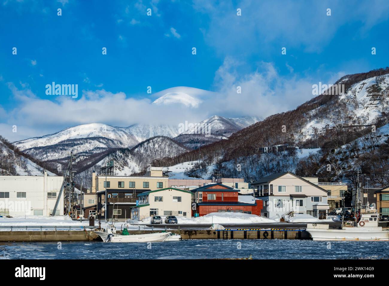 Kleine Stadt an der Küste, mit schneebedeckten Bergen im Hinterland. Rausu, Hokkaido, Japan. Stockfoto