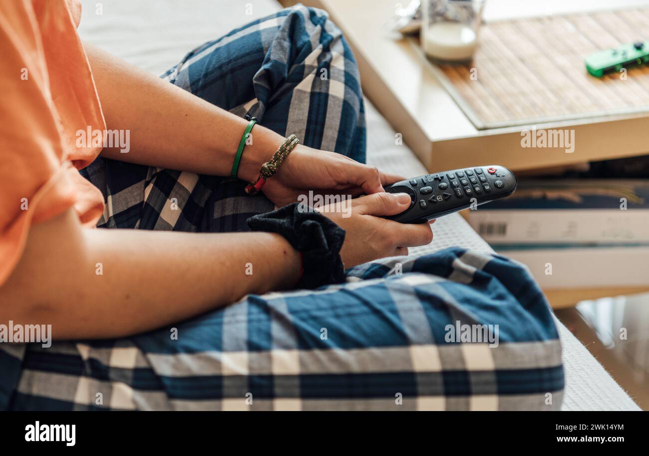 Hände einer nicht erkennbaren Person, die eine Fernbedienung auf dem Sofa hält Stockfoto