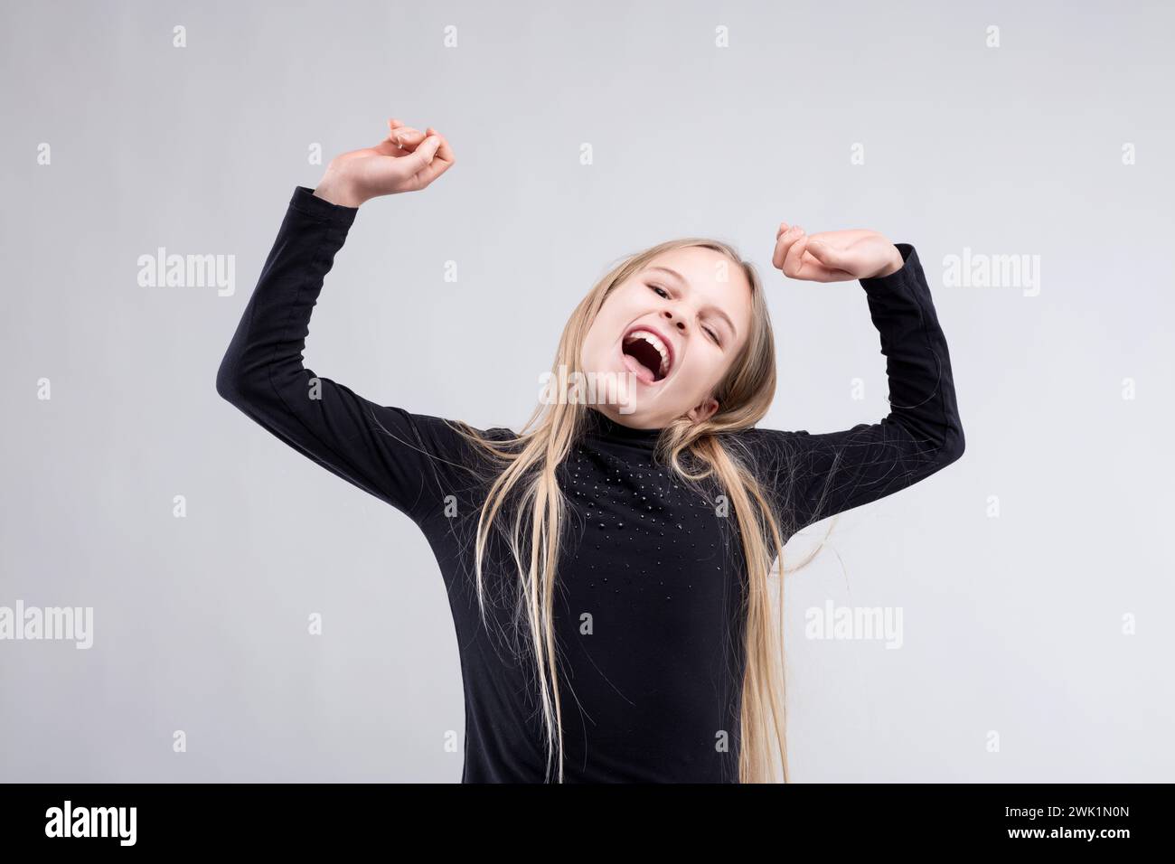 Das überschwängliche junge Mädchen mit erhobenen Armen feiert fröhlich, ihr Lachen spiegelt das Wesen der Lautstärke wider Stockfoto