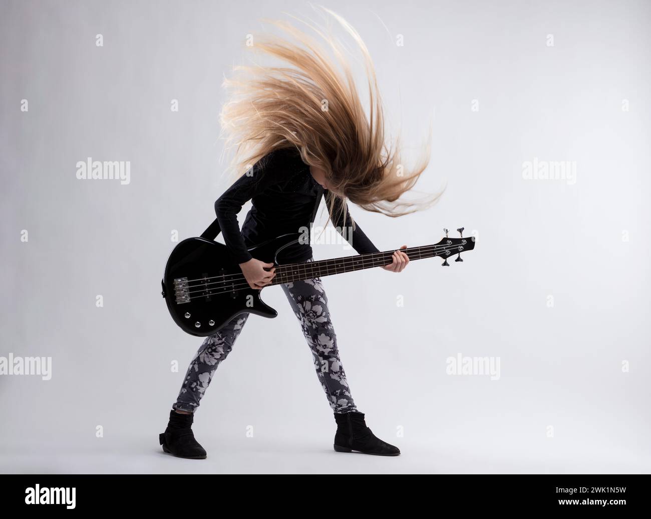 Mit einer Bassgitarre in der Hand spricht die intensive Haarwelle des Mädchens für ihren künstlerischen Antrieb Stockfoto