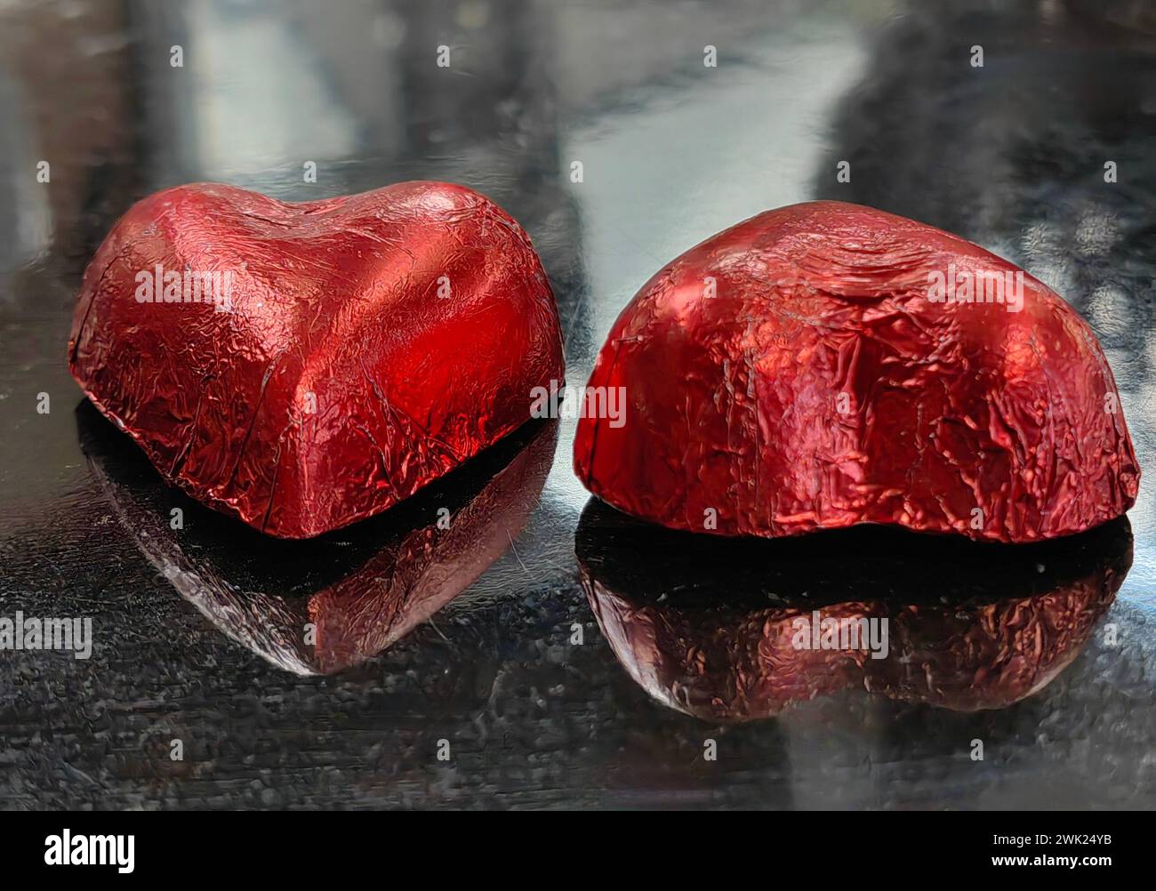 Zuckerdichotomie. Geschlechtsspezifische Reflexionen. Zwei herzförmige Schokoladenbonbons auf schwarzem Tisch, die Mann und Frau symbolisieren. Alles Gute zum Valentinstag. Stockfoto
