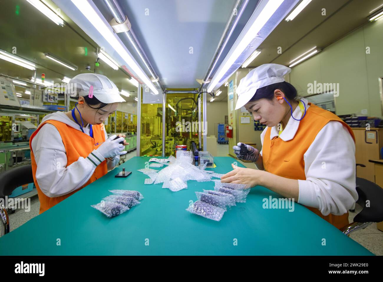 QINGDAO, CHINA - 18. FEBRUAR 2024 - zwei Arbeiter führen Inspektions- und Verpackungsarbeiten in einer Werkstatt eines Automobilelektronikunternehmens in Q durch Stockfoto