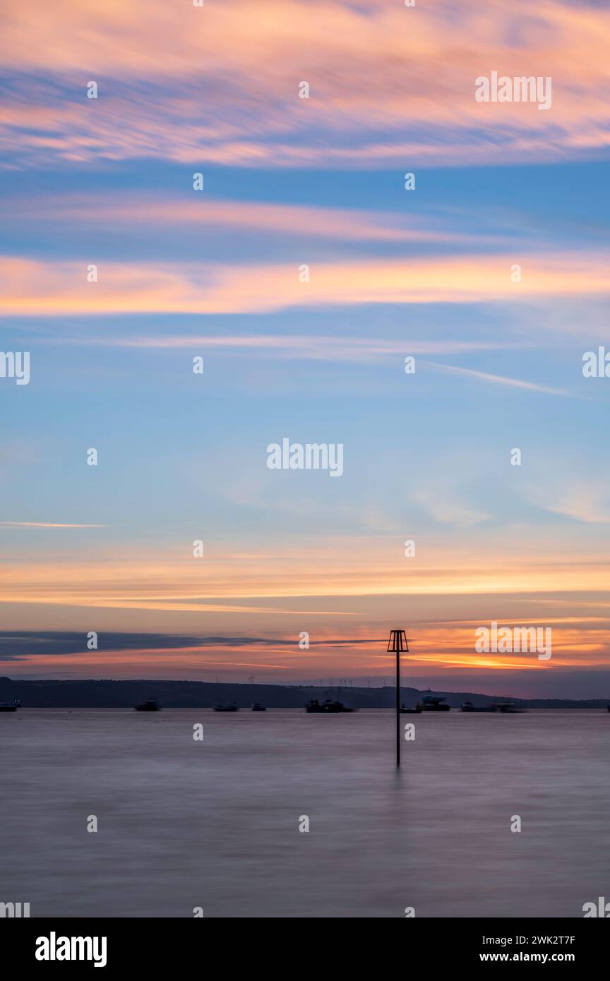 Sommersonnenaufgang über Tenby South Beach, Wales, Großbritannien. Die Sonne geht über einem ruhigen Meer auf und färbt den Himmel orange und rot. Es ist ein einzelner Posten sichtbar Stockfoto