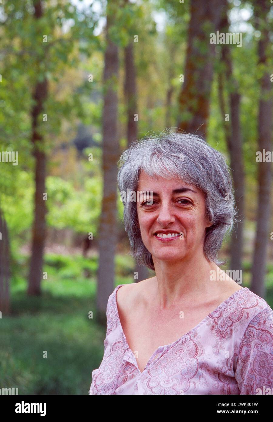 Reife Frau im Wald, lächelt und schaut in die Kamera. Stockfoto