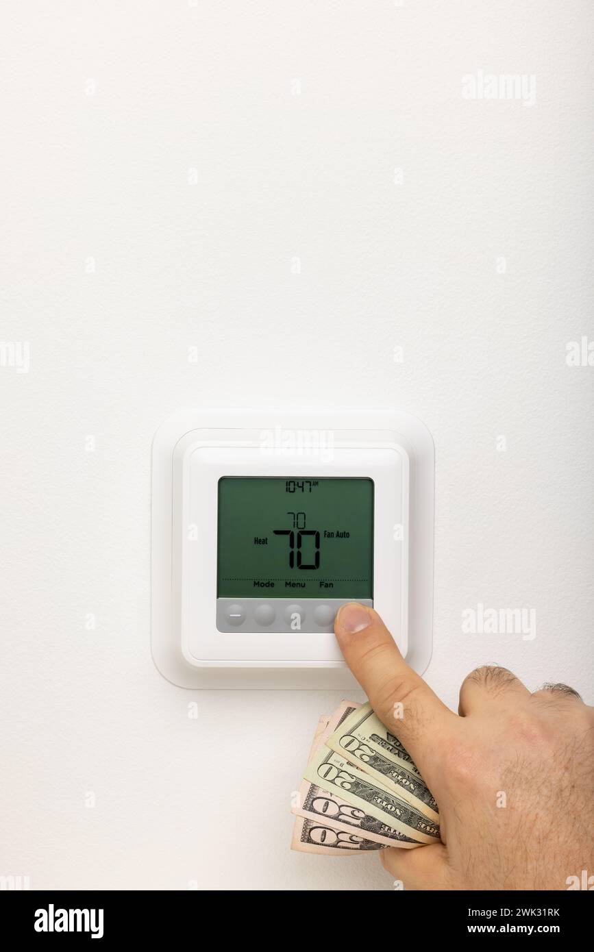 Eine Hand, die Geld hält, um einen Thermostat einzustellen. Stockfoto