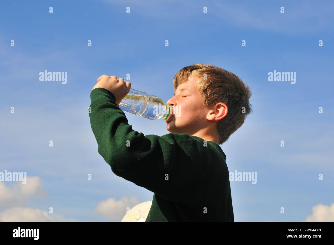 Ein Junge trinkt Wasser aus einer Flasche und die andere Hand hält den Ball Stockfoto