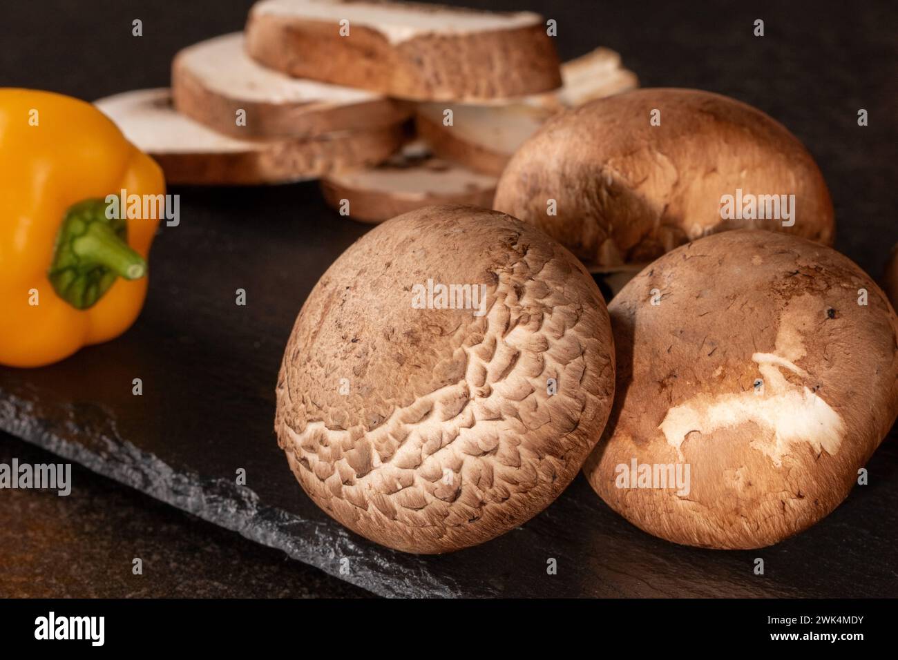 Nahaufnahme frischer ganzer und geschnittener Pilze auf dunklem Hintergrund, perfekt für kulinarische Zutaten und Ernährungskonzepte. Qualitativ hochwertige Bilder Stockfoto