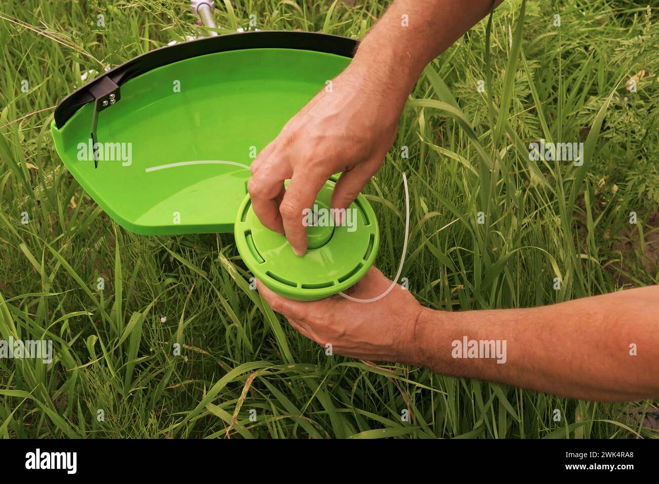 Wartung von Gartenwerkzeugen. Gärtner befestigen auf einer Wiese mit Gras eine Haspel an einem Mäher. Nahaufnahme eines Mannes, der einen Rasenmäher auseinander nimmt, um Teile auszutauschen. Ersetzen der Spule in einem Rasenmäher Stockfoto