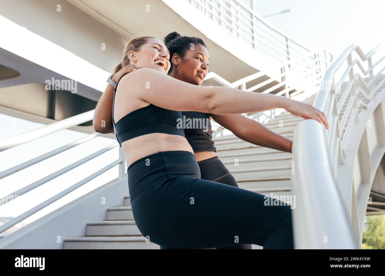 Zwei Sportlerinnen, die nach einem intensiven Workout am Geländer auf der Brücke stehen. Weibliche Freunde in Sportbekleidung, die nach E gute Laune haben Stockfoto