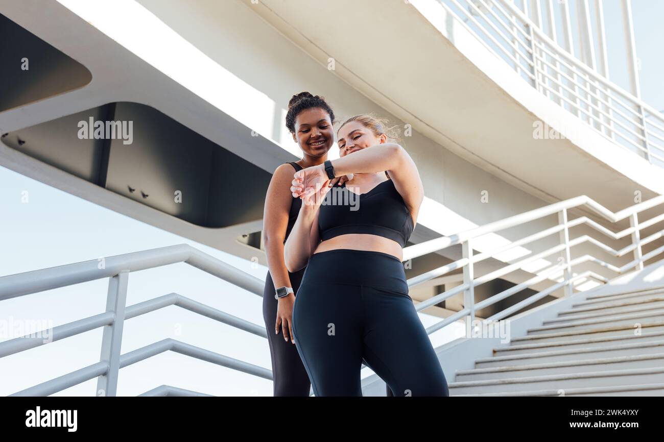Zwei lächelnde weibliche Athleten, die auf die Smartwatch schauen. Frau in Übergröße, die ihrem Fitnessfreund das Ergebnis eines Workouts auf einer Smartwatch zeigt. Stockfoto