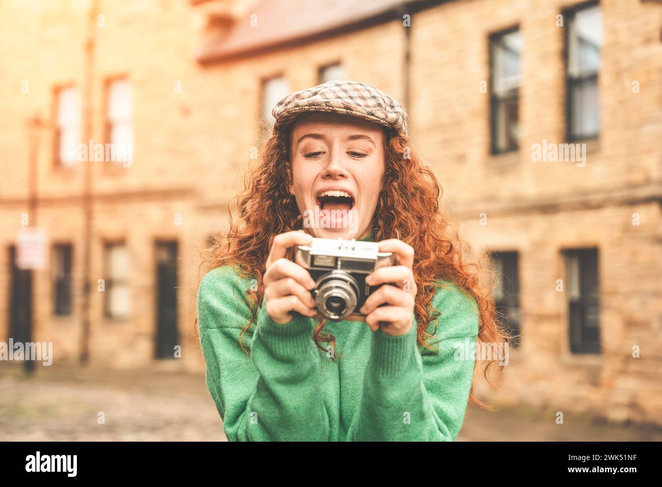 Porträt einer aufgeregten und glücklichen jungen Dame mit rotem Lockenhaar, die eine Altstadt erkundet und Fotos mit einer alten Filmkamera macht Stockfoto