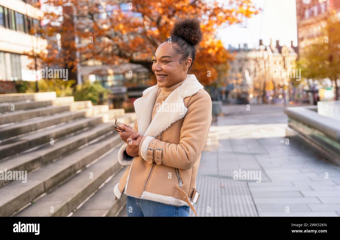 Eine fröhliche Frau, die eine Tasse Kaffee hält. Eine lächelnde, lockige Brünette in einem Pullover trifft Freunde Stockfoto