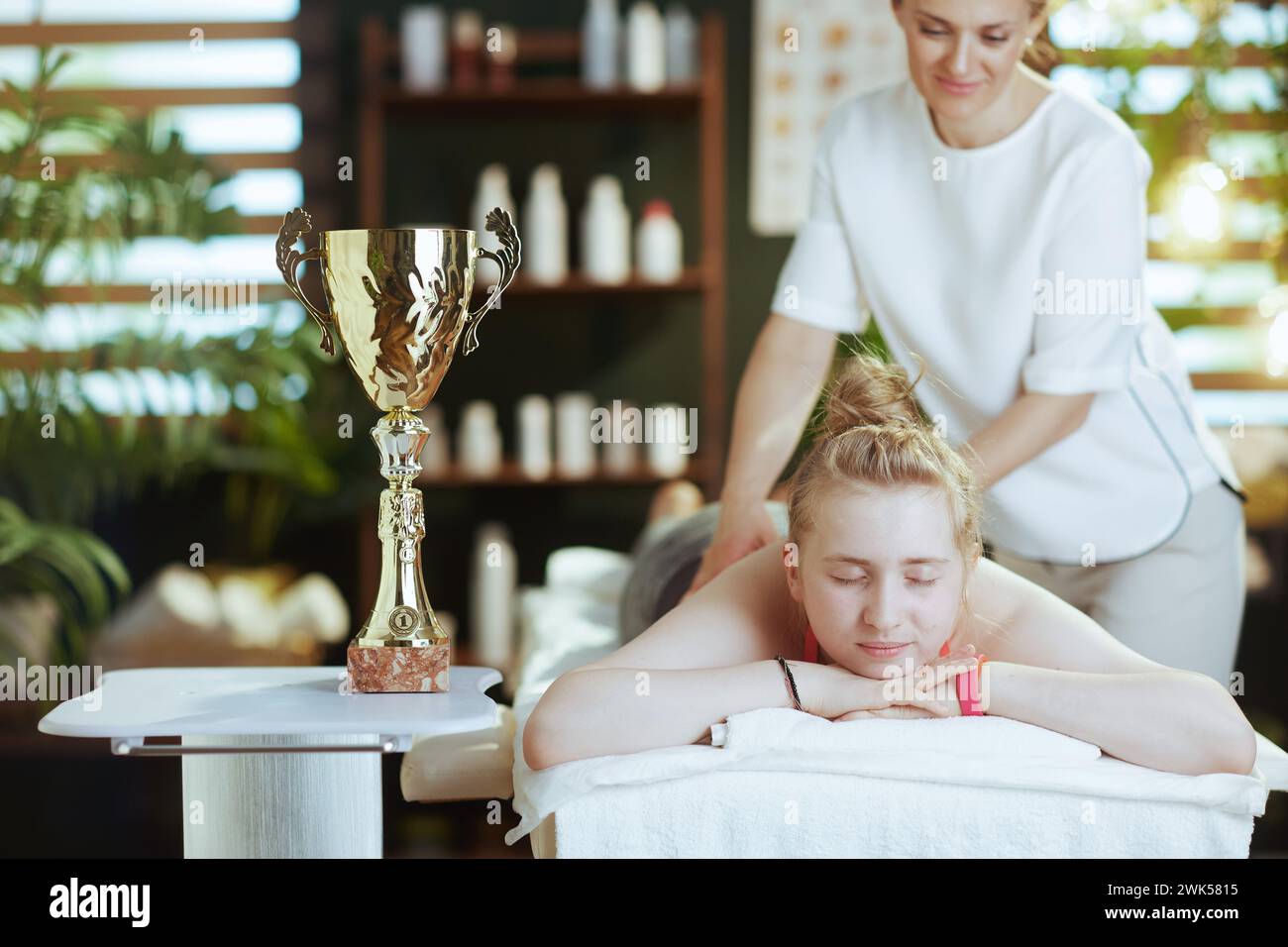 Gesundheitszeit. Weibliche medizinische Massage-Therapeutin in Massageschrank mit Klemmbrett, Teenager-Klientin und Award Cup Make Massage. Stockfoto