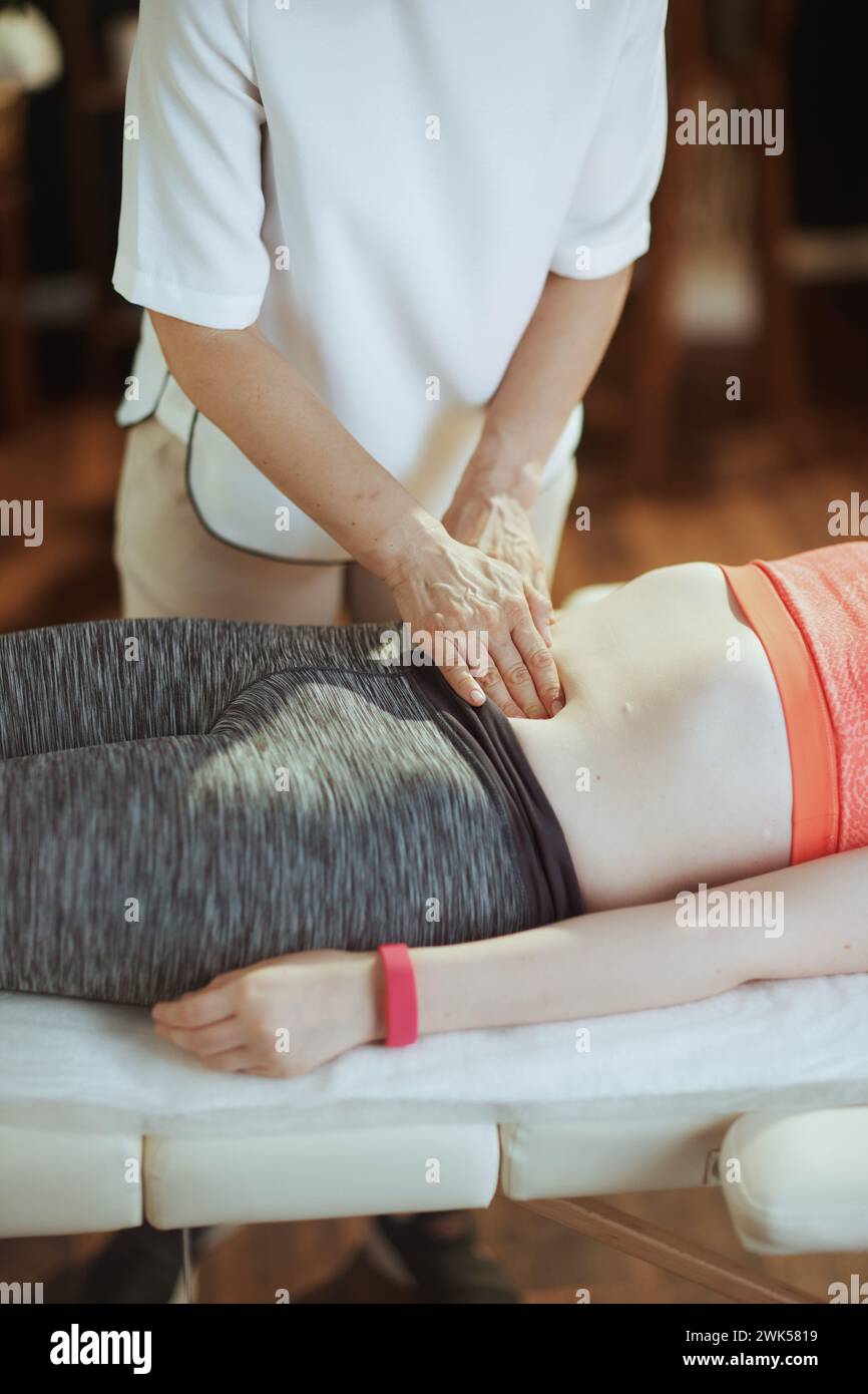 Gesundheitszeit. Nahaufnahme einer medizinischen Massagetherapeutin in Massagekabine mit Teenager-Klientin, die Untersuchung auf Massagetisch durchführt. Stockfoto