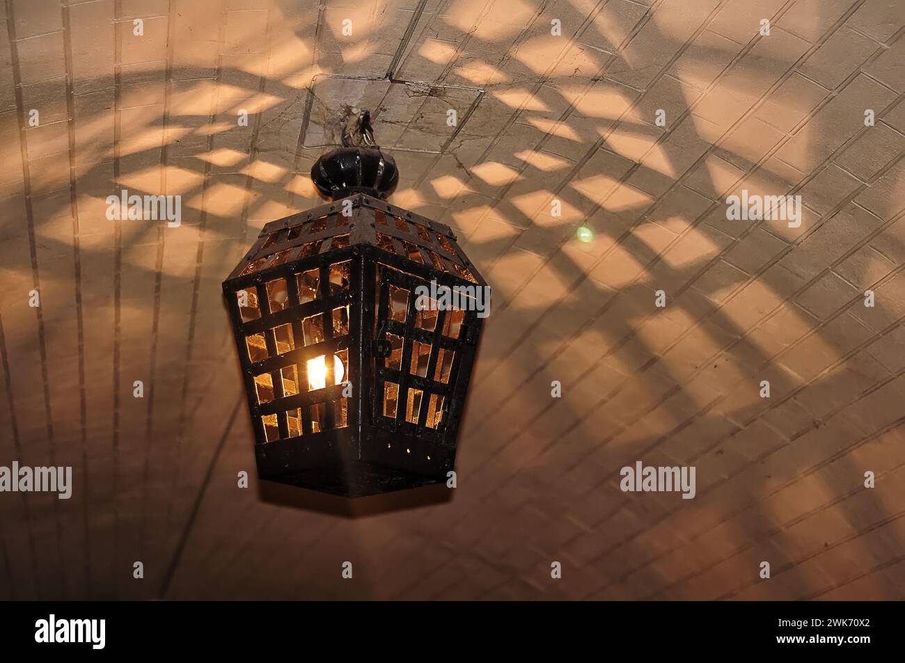 Eine antike Metalllaterne hängt von der Decke. Die gewölbte Decke des Untergeschosses, das Licht der Laterne durch die Gitter Stockfoto