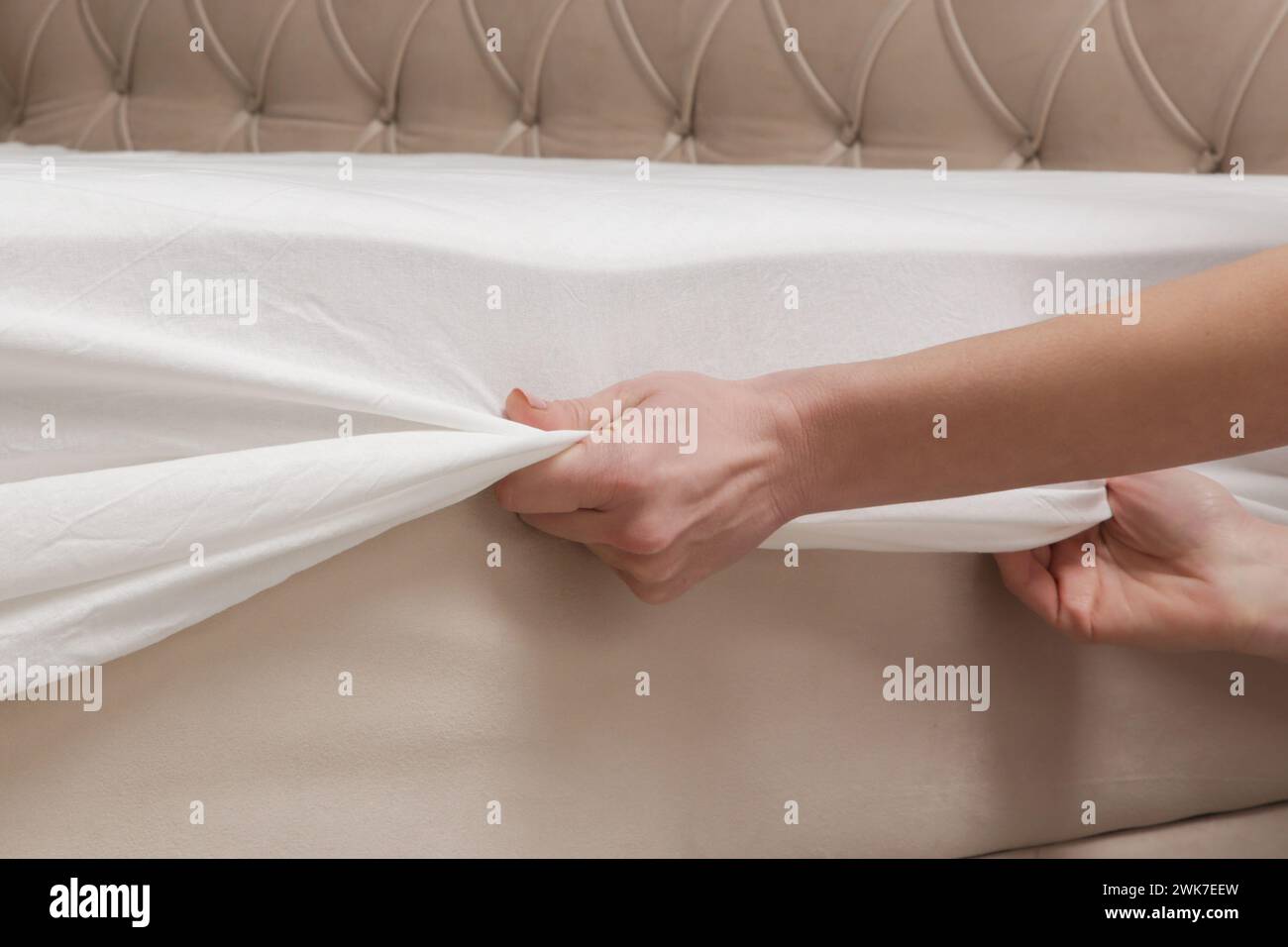 Bettwäsche wechseln. Die Frau zieht ein passendes weißes Baumwolltuch auf eine Matratze, während sie das Bett macht. Stockfoto
