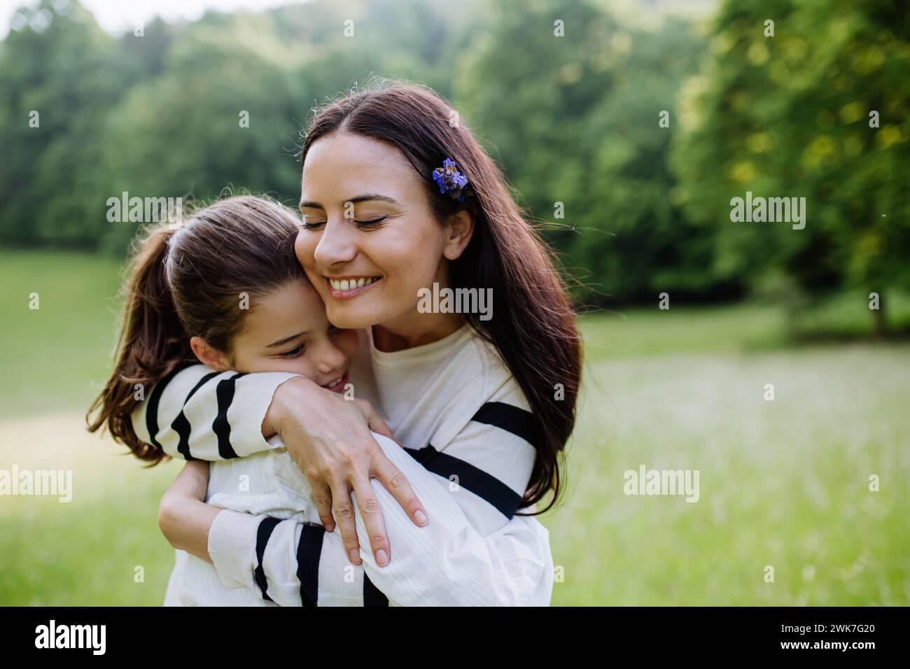 Schöne Mutter mit Tochter, umarmt oder umarmt, sitzt im Gras auf der Wiese. Muttertag und mütterliche Liebe. Stockfoto