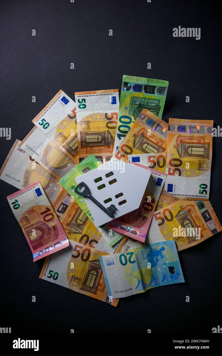 Ein großer Haufen Euro-Geld und ein weißes Holzhaus und ein Schlüssel auf schwarzem Hintergrund - von oben. Stockfoto