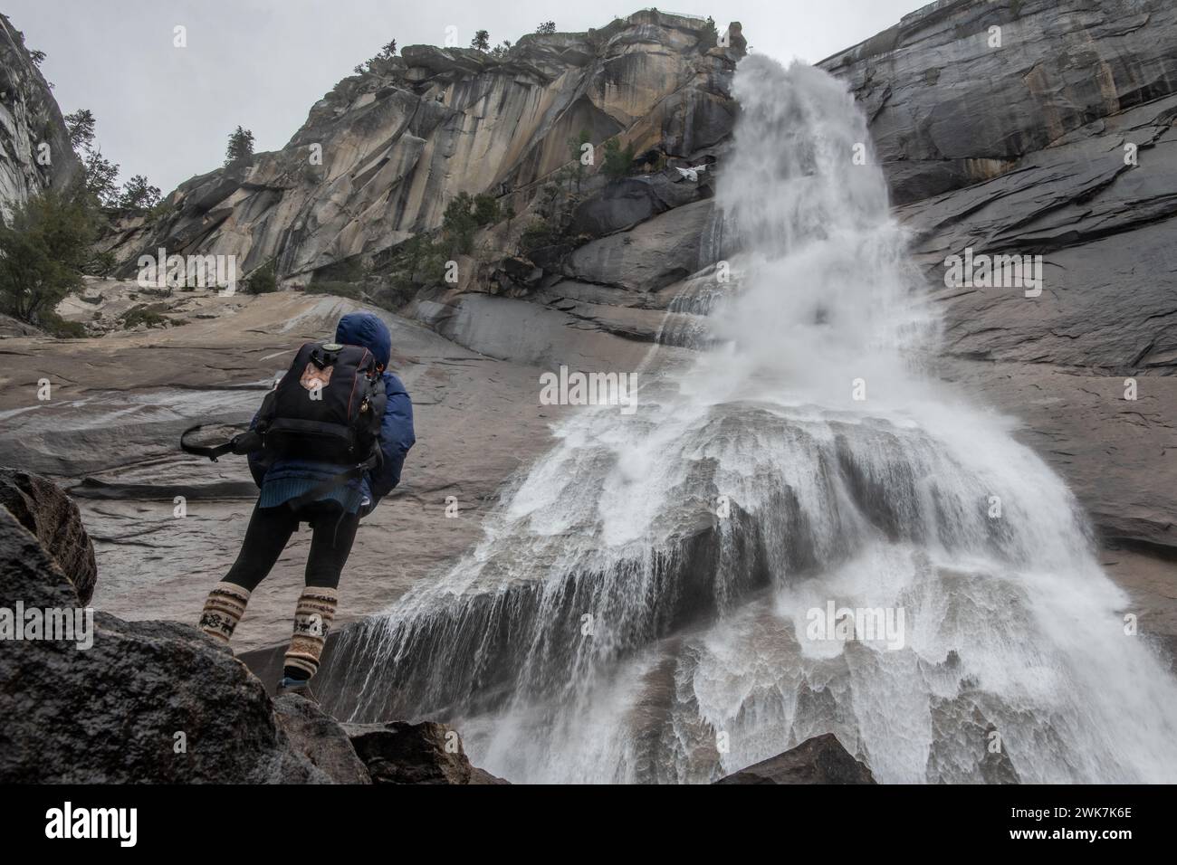 Eine Wanderer steht unter einem Wasserfall im Yosemite-Nationalpark in den Sierra Nevada Mountains in Kalifornien, USA. Stockfoto