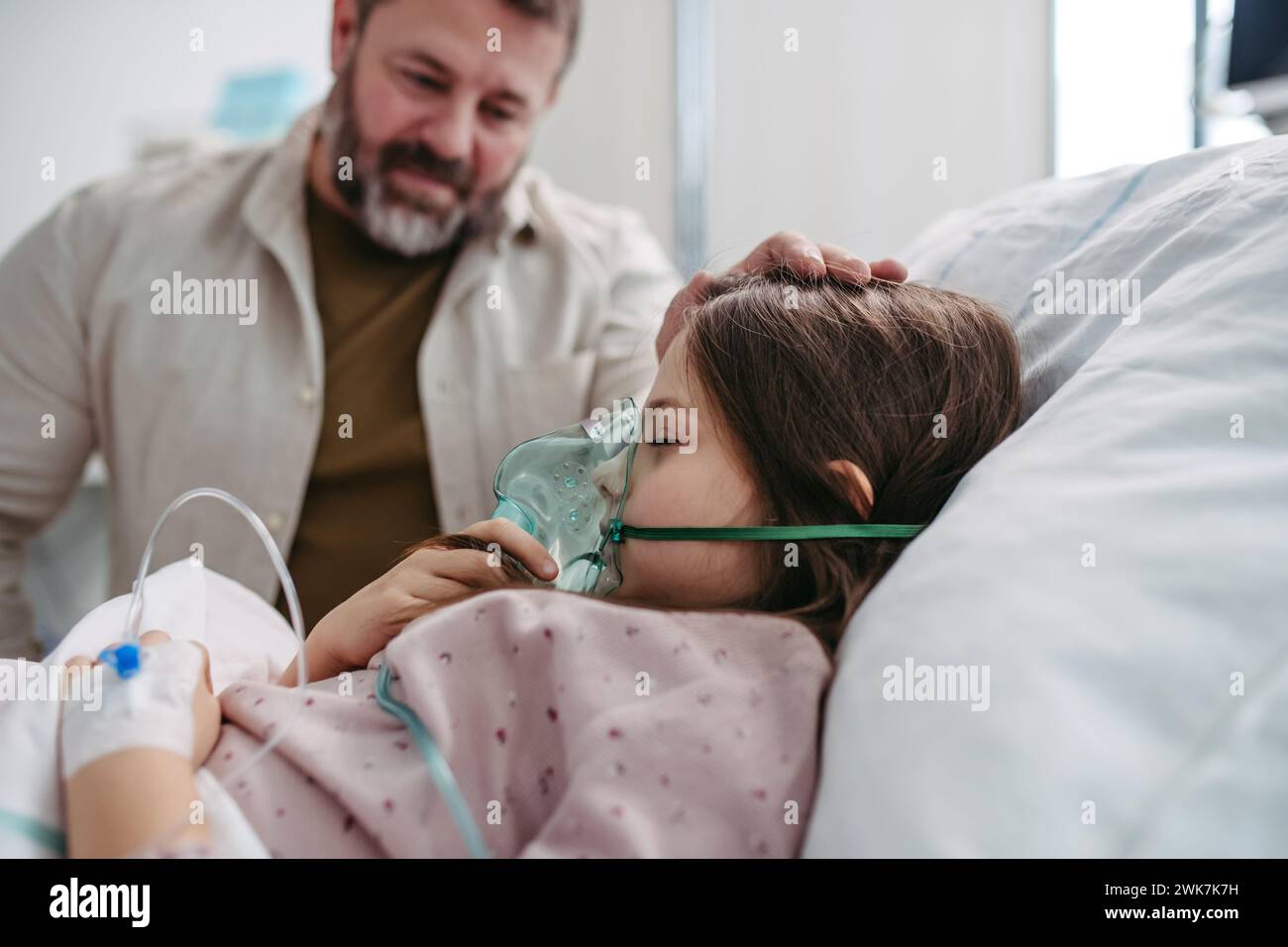 Vater hält die Hand seiner Tochter im Krankenhausbett. Kind im Krankenhausbett mit Sauerstoffmaske im Gesicht auf der Intensivstation. Stockfoto