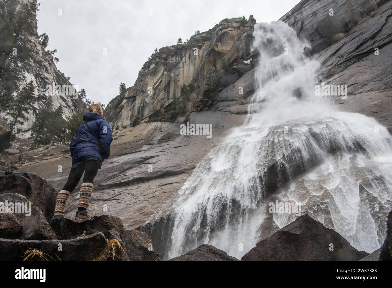 Eine Wanderer steht unter einem Wasserfall im Yosemite-Nationalpark in den Sierra Nevada Mountains in Kalifornien, USA. Stockfoto