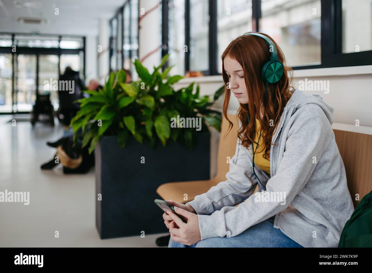 Teenager-Mädchen wartet im Krankenhausflur, hört Musik über Kopfhörer. Jugendlicher Patient kommt zur Untersuchung ins Krankenhaus. Stockfoto