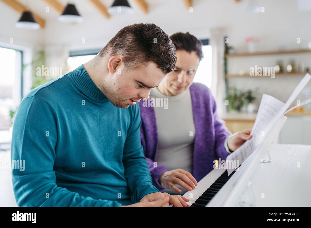 Junger Mann mit Down-Syndrom und seine Mutter spielt am Klavier und macht zu Hause Musik. Stockfoto