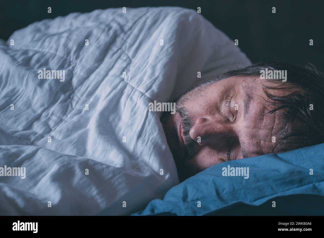 Müder schlafender Erwachsener, männlich in einem Bett auf blauem Kissen, selektiver Fokus Stockfoto