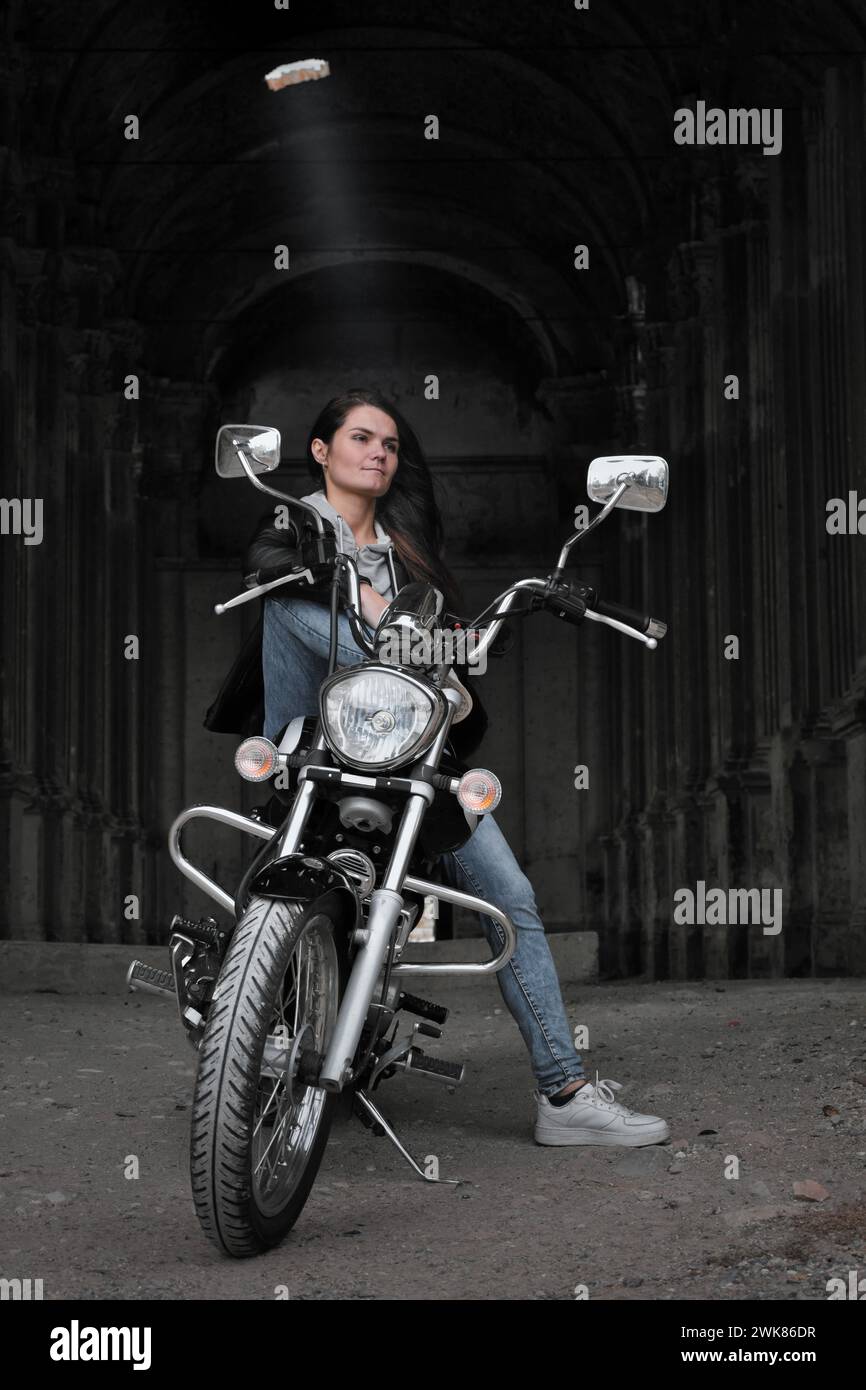 Eine junge Frau in Einer Lederjacke auf Einem Motorrad in einem verlassenen Schloss Stockfoto