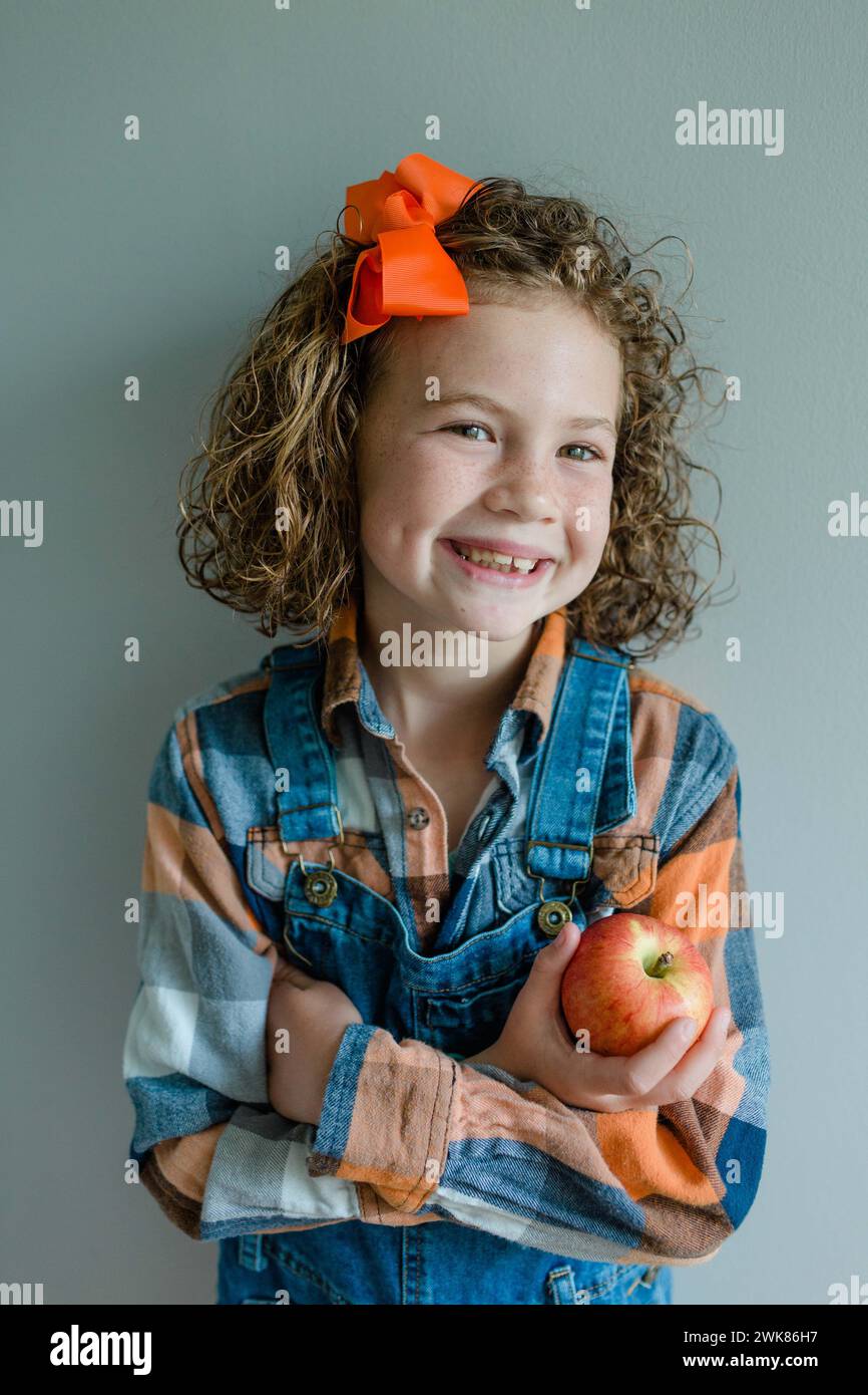 Das kleine Mädchen mit lockigen Haaren trägt einen Overall mit einem Apfel Stockfoto