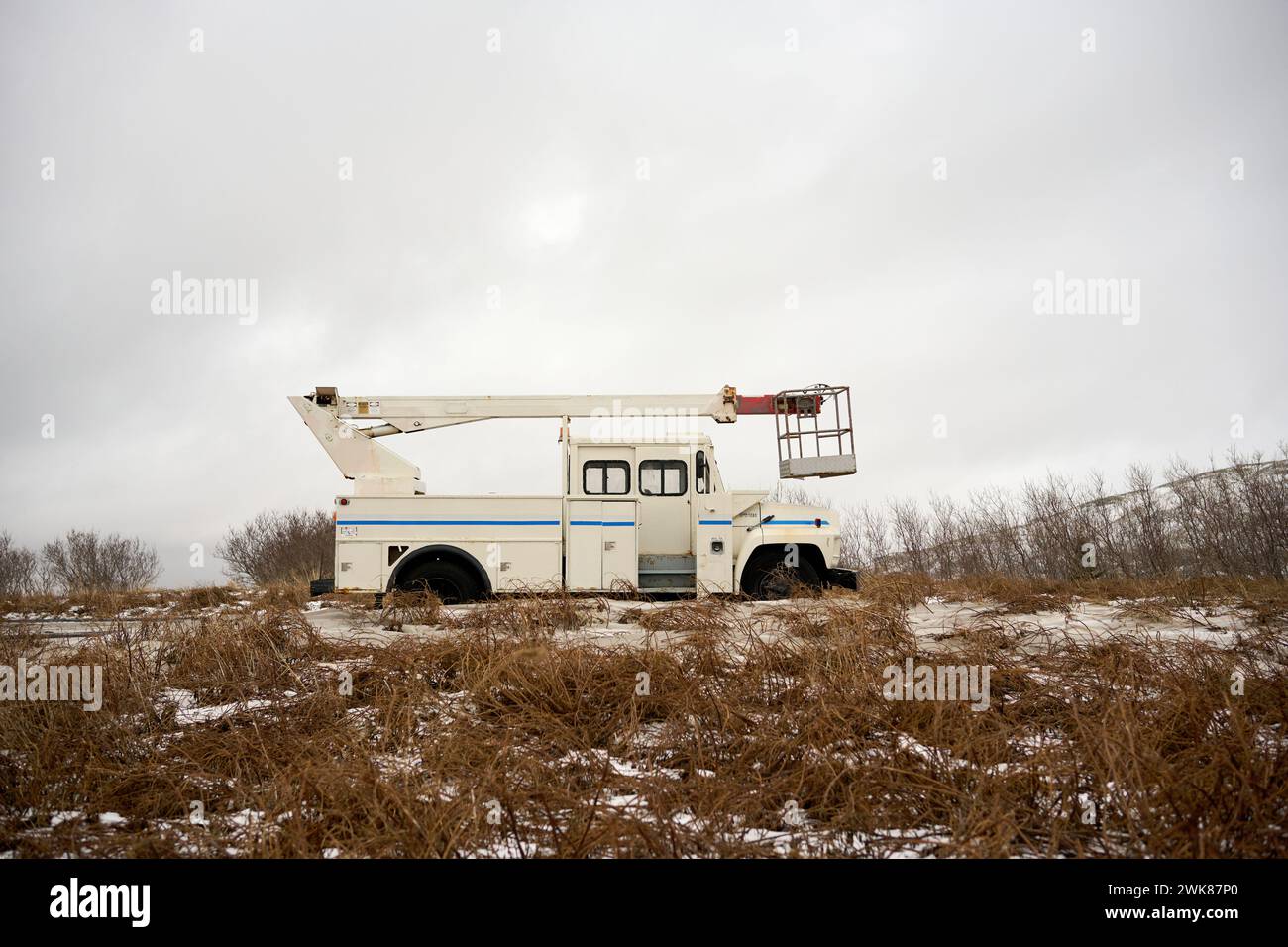 Kranwagen mit Auslegerhubkran auf einem verschneiten, trockenen Grasfeld geparkt Stockfoto