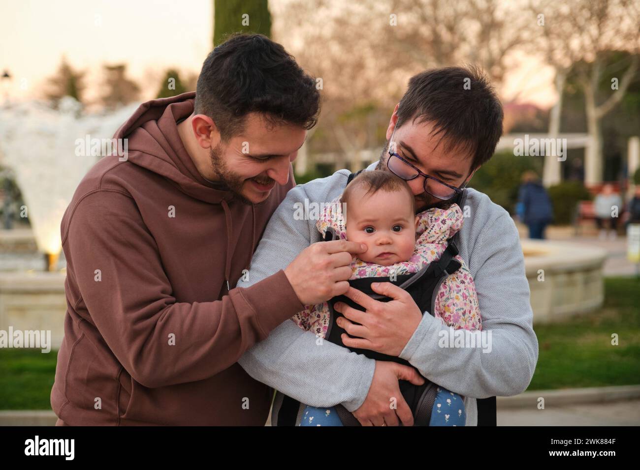 Homosexuelles glückliches Paar, das mit ihrem Baby in einer Babytrage spielt. Stockfoto