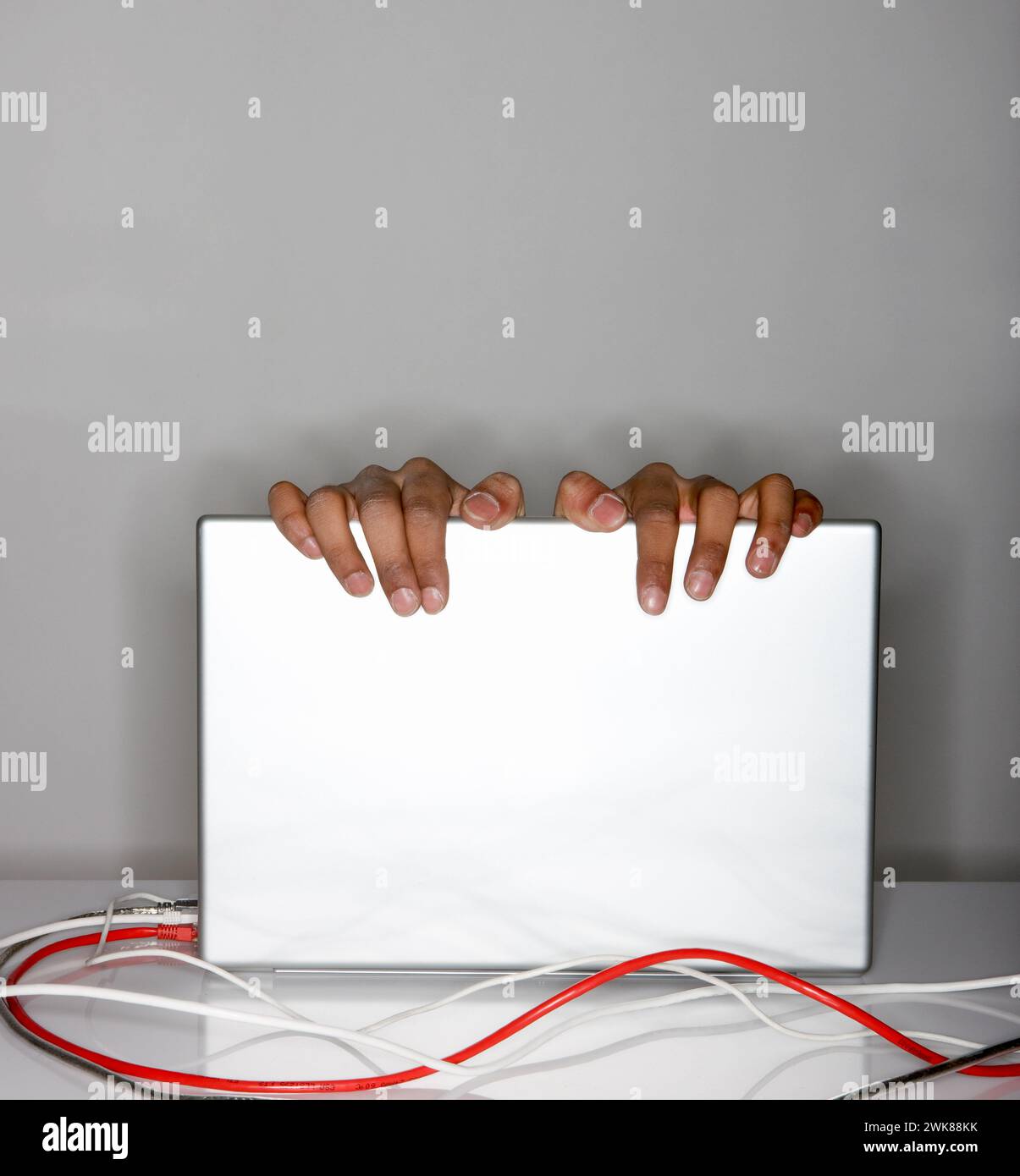 Finger hängen über dem Laptop-Bildschirm, rote und graue Kabel verlegen sich Stockfoto
