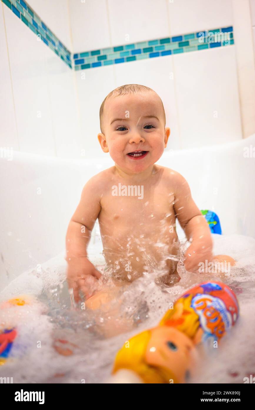 Glücklicher, lächelnder Junge, der im Badewasser mit matey-Bubble-Bad spritzt Stockfoto