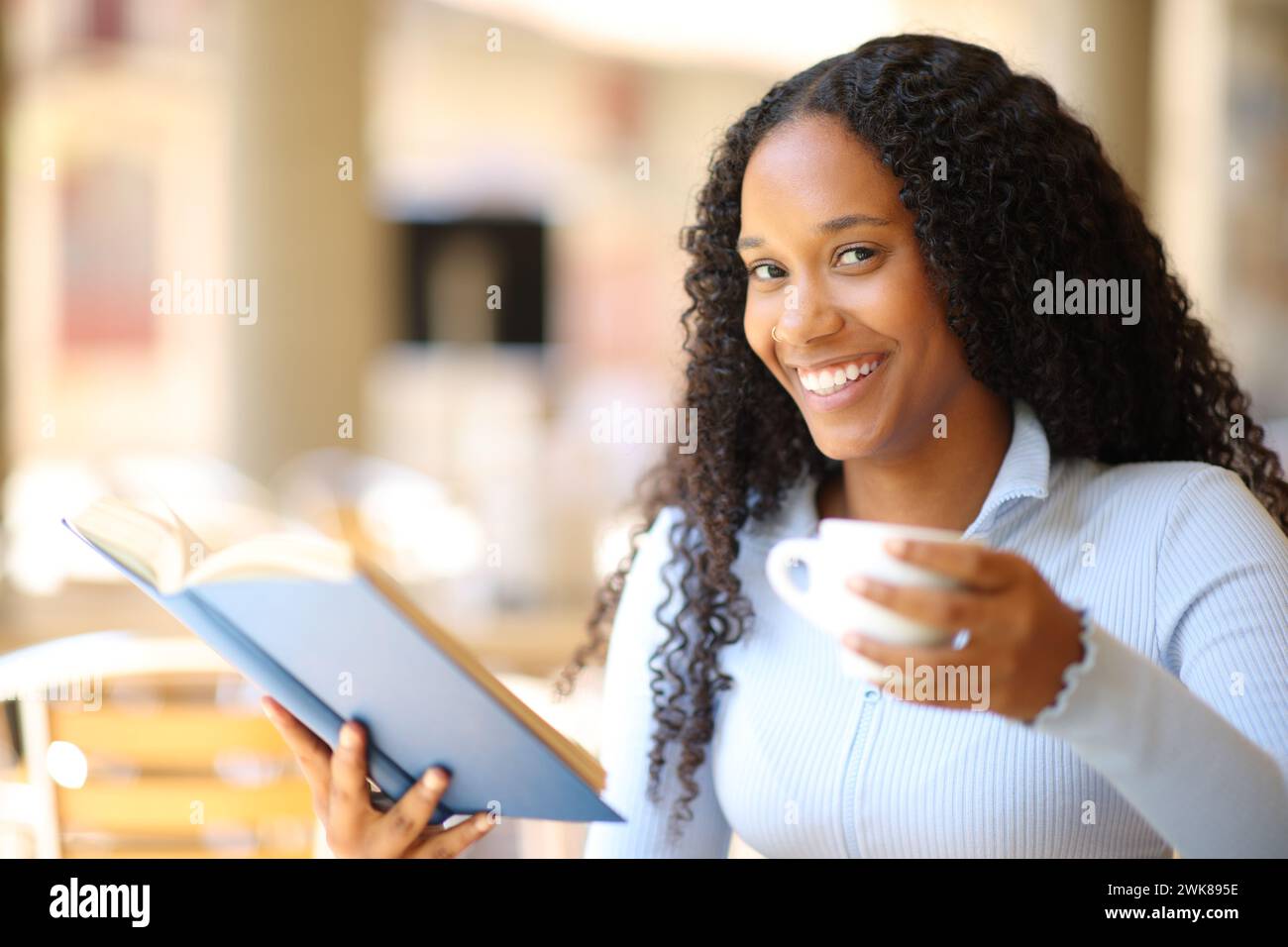 Glückliche schwarze Frau liest ein Papierbuch und trinkt Kaffee auf einer Bar-Terrasse Stockfoto